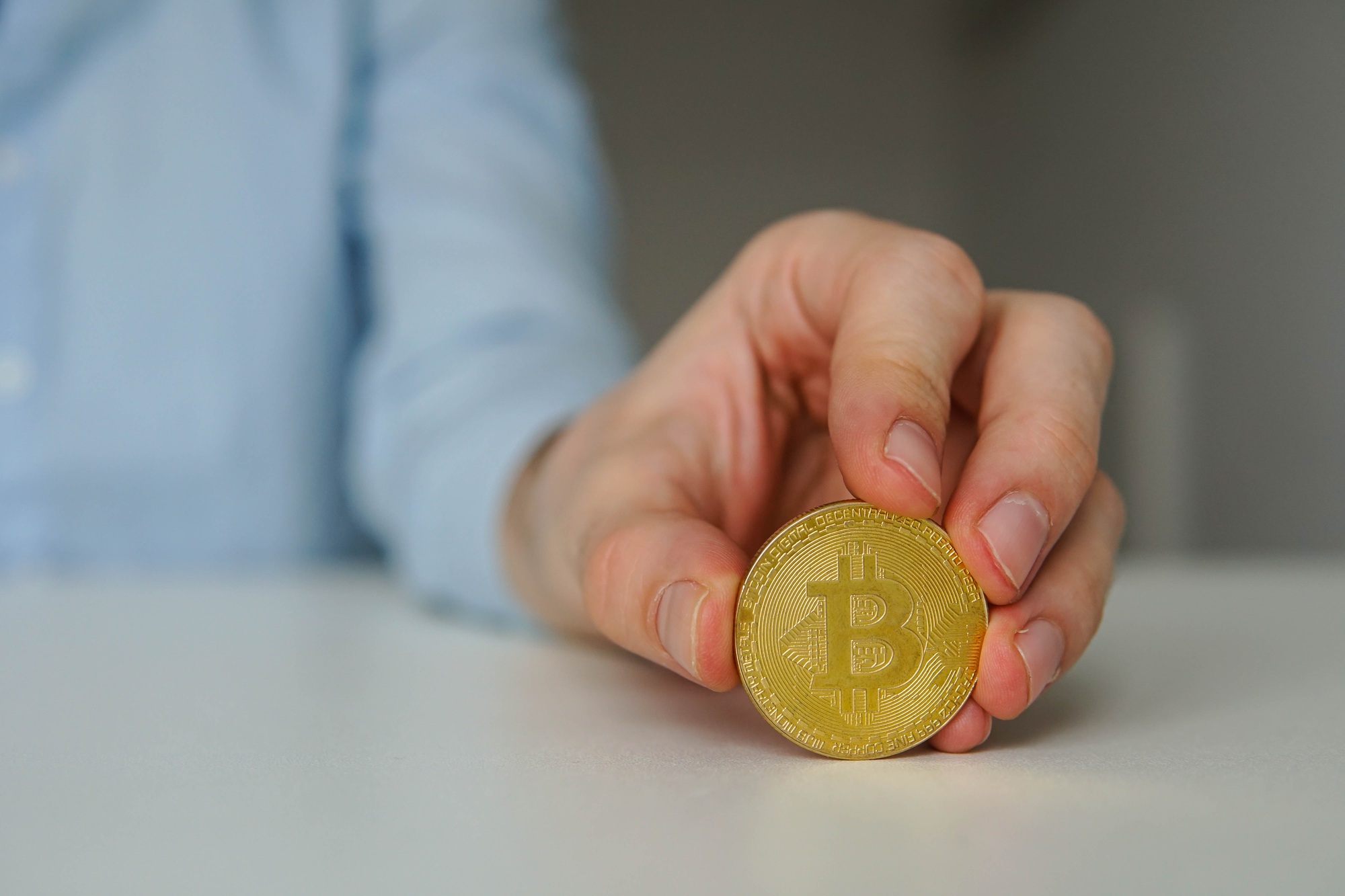 Young man crypto trader holding golden bitcoin on the table.